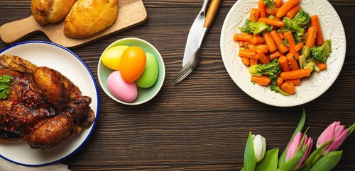 Easter food on dark rustic table: pastel colored eggs, roasted chicken and vegetables, buns and