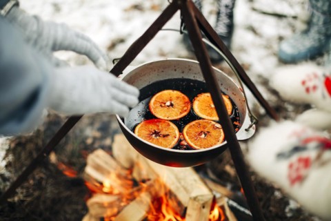 From above traditional mulled wine with slices of orange preparing in pot over burning logs in