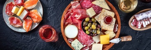 Italian antipasti or Spanish tapas panorama on a black background. Gourmet cold meat and cheese