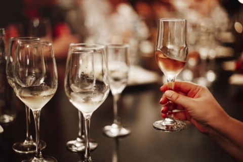 Glasses with different types of wine and human hands holding wine glasses in the background.