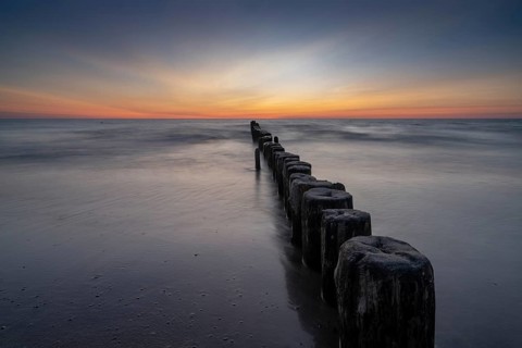 long exposure view of an ocean sunset with sandy beach and wooden pylon storm groin in the