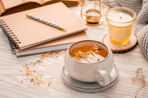 Hot herbal tea with notepad, candle, book and blanket. Cozy and hygge lifestyle