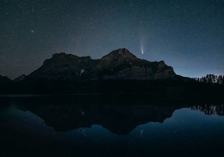 Night sky with stars over a mountain and its reflection in a calm lake, silhouette and a visible