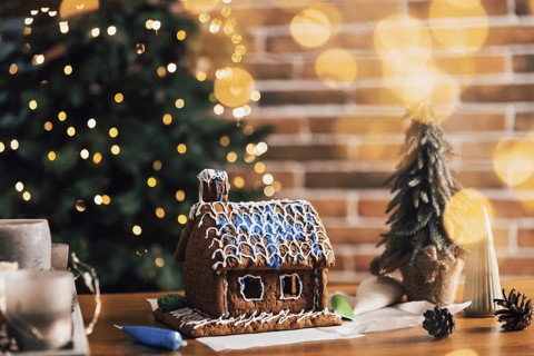Little homemade gingerbread house standing on table with decorations, candles in living room