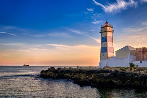 Dramatic sunset on sea shore and Santa Marta lighthouse in Cascais, Portugal. Colorful sky, clouds,