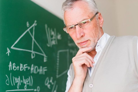 Aged professor standing near chalkboard classroom