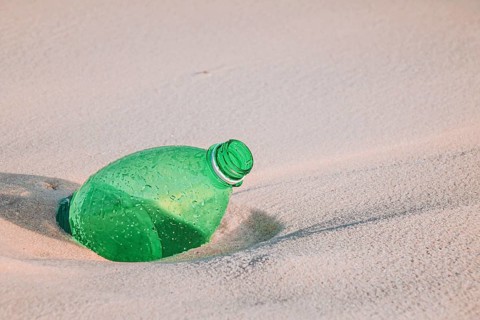Green plastic bottle on sandy beach highlighting environmental pollution