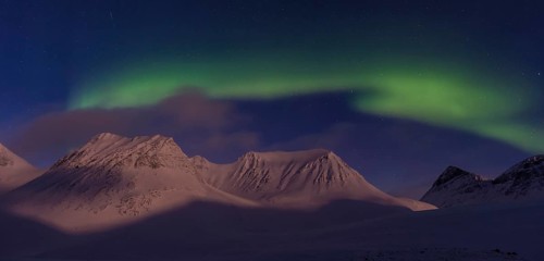 Northern Lights (Aurora borealis) over moonlit mountains in the valley Stuor Reaiddavaggi,