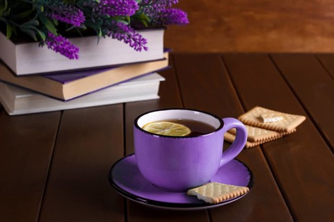 Cup of tea with lemon and cookies next to old books over vintage wooden background