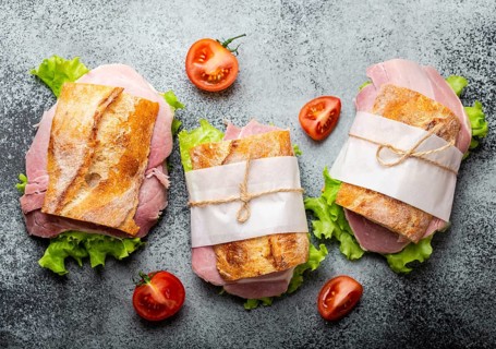 Fresh ciabatta sandwiches with ham, cheese, lettuce, tomatoes on stone concrete background,