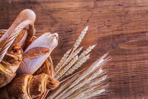 Close up view on baguettes and croissants in wicker basket with ears of wheat on old wooden boards
