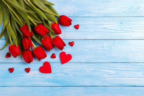 Red tulips and hearts on blue wooden table. Top view with copy space