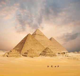 Dramatic sunset behind all distant Egyptian Pyramids together with line of camels walking in