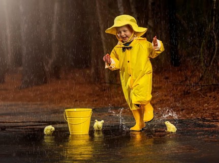 A small child plays in the rain while little chicks try to get a drink of water