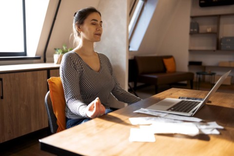 Stress relief during freelance work. Brunette woman freelancer sitting in lotus pose and meditating