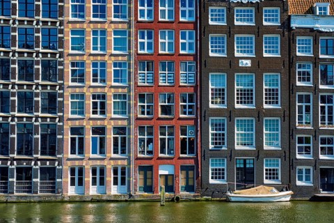 Row of typical houses and boat on Amsterdam canal Damrak with reflection. Amsterdam, Netherlands