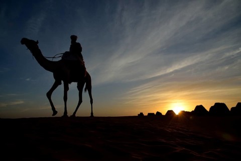 Man riding a camel at sunset at the pyramids of the north cemetery Meroe, Nubia, Nahr an-Nil,