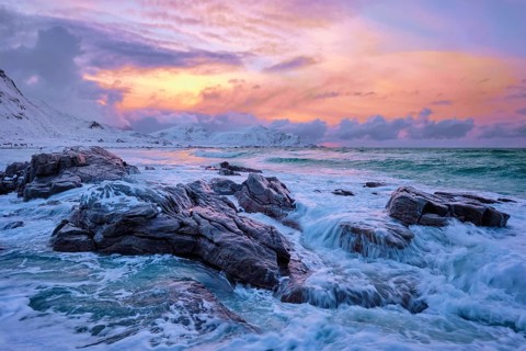 Waves of Norwegian sea on rocky coast in fjord on sunset with sun. Skagsanden beach, Lofoten
