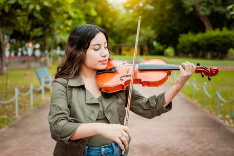 Woman playing the violin in the street. Close up of violinist girl playing in a park. Artist woman