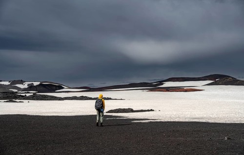 Hikers in snow-covered volcanic landscape with volcanic sand and petrified lava, crater of Askja