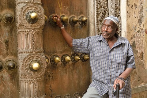 Elderly man leaning against a wooden door in the historic town centre, Zanzibar City, Zanzibar,