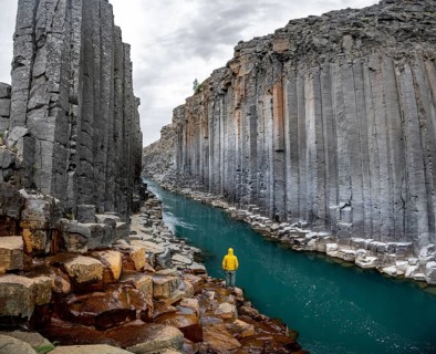 Tourist standing by the river in Stuðlagil Canyon, turquoise blue river between basalt columns,