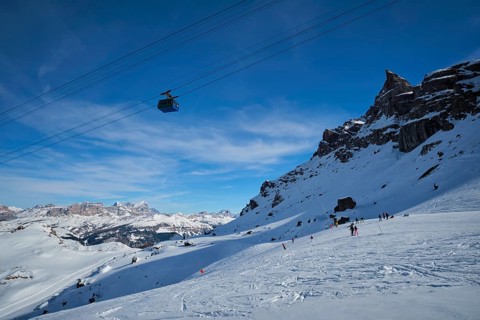 View of a ski resort piste with people skiing in Dolomites in Italy with cable car ski lift. Ski