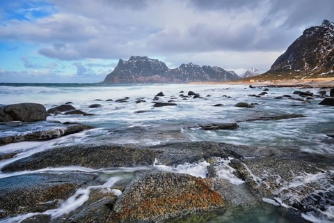 Rocks on beach of fjord of Norwegian sea in winter with snow. Utakliev beach, Lofoten islands,