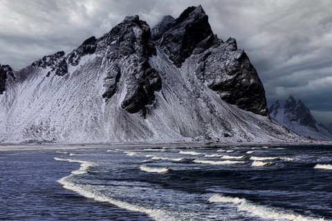White foamy waves on the beach of Stokkness, behind snowy rocky slopes of Vestrahorn, near Höfn,