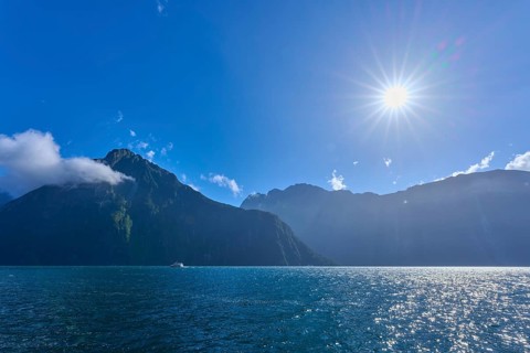 Bright sun over mountains and an expanse of water, summer, Milford Sound, Te Anau, Fiordland