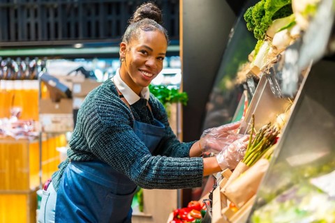 African american saleswoman wearing plastic gloves arranging organic asparagus at the vegetable