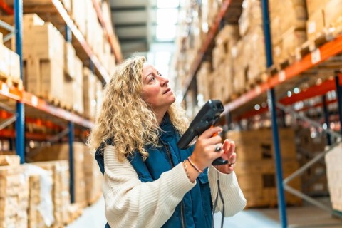 Woman worker looking up while scanning the barcode of packages in a warehouse