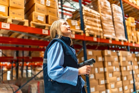 Blonde woman manual worker in waistcoat scanning parcels in a warehouse