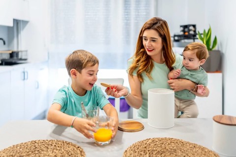 Happy woman feeding her son while holding a baby during breakfast at home