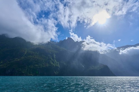 Sunshine over mountains with partial cloud cover and blue water, summer, Milford Sound, Te Anau,