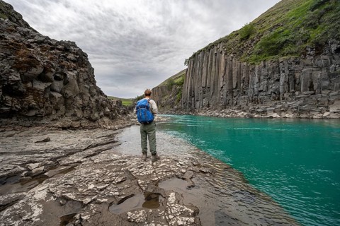 Tourist standing by the river in Stuðlagil Canyon, turquoise blue river between basalt columns,