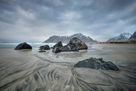 Rocks on beach of fjord of Norwegian sea in winter with snow. Skagsanden beach, Lofoten islands,