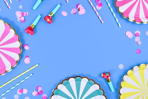 Party flat lay with paper plates, drinking straws and confetti on blue background with copy space