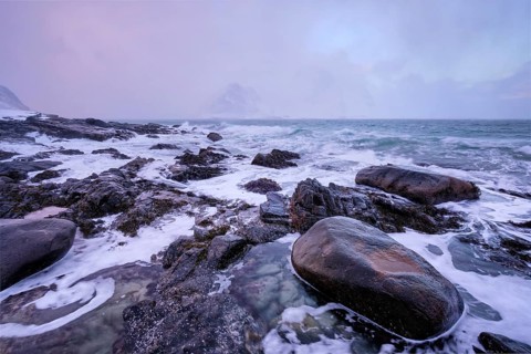 Beach of Norwegian sea on rocky coast in fjord on sunset in winter. Vareid beach, Lofoten islands,