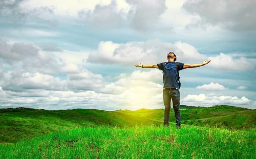 Adventurous man spreading his arms in the countryside. Man with backpack on a hill spreading his