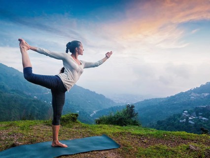 Woman doing yoga asana Natarajasana, Lord of the dance pose outdoors at waterfall in Himalayas
