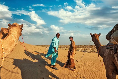 Rajasthan travel background, two indian cameleers (camel drivers) with camels in dunes of Thar