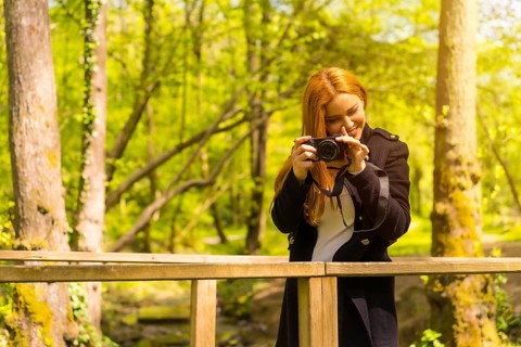 Woman photographer with a black jacket enjoying in an autumn park, smiling and enjoying taking