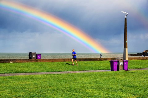 Pedestrians and joggers on seafront promenade, dramatic cloudy sky with rainbow, Bray, Wicklow,