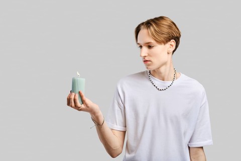 Young man holds candle in hand over grey studio background
