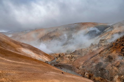 Steaming stream between colourful rhyolite mountains and snowfields, Hveradalir geothermal area,