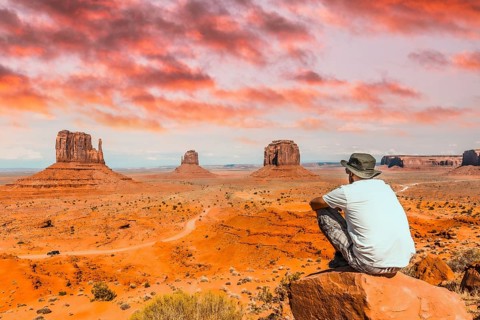 A young boy with white t-shirt sitting in the center of the photo on a stone in the Monument Valley