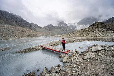 Mountaineer on a bridge over a glacial river of the glacier Glacier de Cheilon, Valais, Western