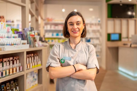 Proud young woman pharmacist standing with arms crossed smiling at camera in the store