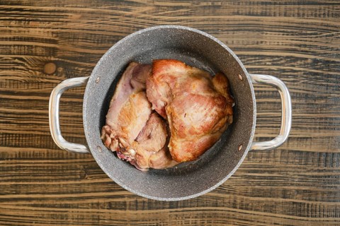 Tender, cooked turkey meat sit in a silver pot on a rustic wooden table, showcasing their golden